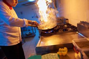 chef en la cocina del hotel prepara comida con fuego foto