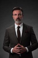 Portrait of a stylish elegant senior businessman with a beard and casual business clothes in photo studio isolated on dark background gesturing with hands