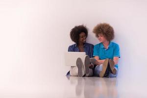 multiethnic couple sitting on the floor with a laptop and tablet photo