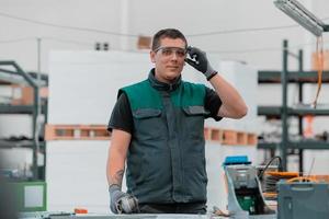 interior de fábrica de ingeniería de industria pesada con trabajador industrial usando amoladora angular y cortando un tubo de metal. contratista en estructuras metálicas de fabricación de cascos y uniformes de seguridad. foto