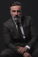 Portrait of adult businessman wearing trendy suit and sitting in modern studio on stylish chair against the black background photo