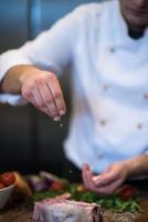 chef poniendo sal en una jugosa rebanada de bistec crudo foto