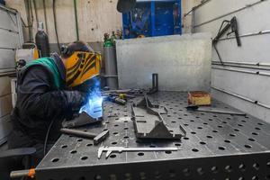 soldador profesional realiza trabajos con piezas metálicas en fábrica, chispas y electricidad. pancarta de trabajadores de la industria. foto