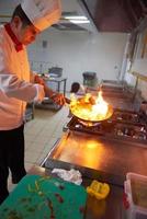chef en la cocina del hotel prepara comida con fuego foto