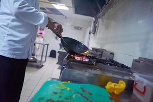 chef en la cocina del hotel prepara comida con fuego foto