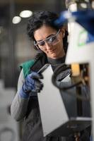 mujer trabajadora con gafas de seguridad controla la máquina de torno para perforar componentes. fábrica de fabricación industrial de torno de metal foto