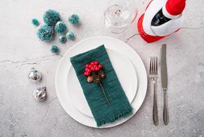 Christmas table setting with white dishware, silverware and red and green decorations on white wooden background. Top view. photo