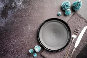 Christmas table setting with black dishware, silverware and green decorations on dark background. Top view. photo