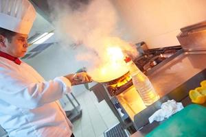 chef en la cocina del hotel prepara comida con fuego foto