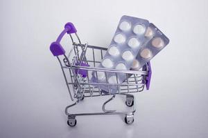 Mini decorative shopping cart with two blisters of tablets on white background. photo