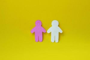 Two silhouettes of a people carved from white and pink paper on yellow background. photo