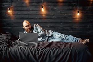 estilo de vida exitoso hombre independiente con barba logra un nuevo objetivo con una computadora portátil en el interior del loft foto