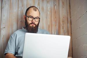 hombre barbudo con gafas trabajando en una computadora portátil. foto