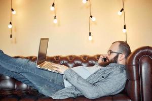 estilo de vida exitoso hombre independiente con barba logra un nuevo objetivo con una computadora portátil en el interior del loft foto