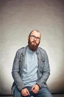 estilo de vida exitoso joven con gafas, barba, chaqueta de mezclilla de moda mirando hacia adelante, retrato masculino en el estudio sobre un fondo uniforme. foto