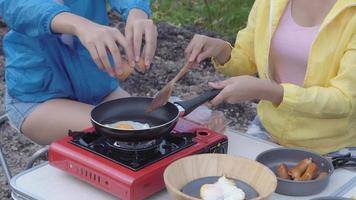 Happy with group of friends picnic with cooking food in summer, two woman enjoy and fun camping journey adventure for leisure and fried egg together in vacation, backpack to travel in holiday. video
