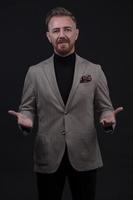 Portrait of a stylish elegant senior businessman with a beard and casual business clothes in photo studio isolated on dark background gesturing with hands