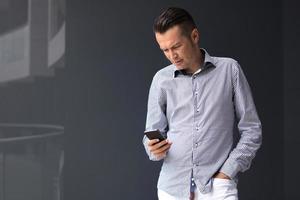 Businessman text messaging on mobile phone against the wall.