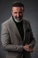 Portrait of a stylish elegant senior businessman with a beard and casual business clothes in photo studio isolated on dark background gesturing with hands