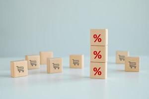 Percentage sign on stack of blocks and trolley cart icon on wooden cube, Sale discount and Online shopping business concept. Consumer society trend. Sale volume increase make business grow. photo