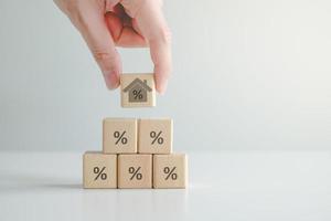 House and property investment and asset management concept. Interest rates, loan mortgage, house tax. Hand holding house with percentage sign on wooden block from wooden block with percent icon. photo