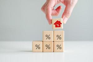 House and property investment and asset management concept. Interest rates, loan mortgage, house tax. Hand holding house icon with percent sign from stack of blocks with percentage icon photo