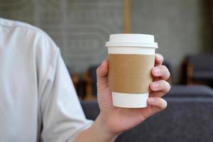 mano de hombre sosteniendo una taza de papel marrón de bebida caliente en la cafetería. Taza de bebida caliente para llevar. foto