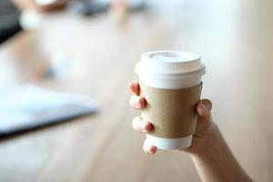 Hand holding paper cup of hot coffee in cafe. Take away hot drinks. photo