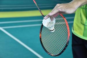 Badminton player holds racket and white cream shuttlecock in front of the net before serving it to another side of the court. photo