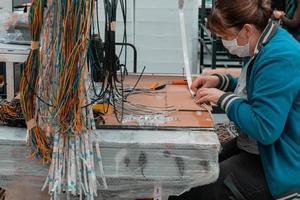 trabajador industrial que usa una máscara facial debido a una pandemia de coronavirus que suelda cables del equipo de producción de la fábrica foto