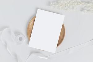 tarjeta de felicitación o tarjeta de invitación con hojas de flores secas blancas sobre placa de madera o bandeja de fondo blanco, vista superior foto