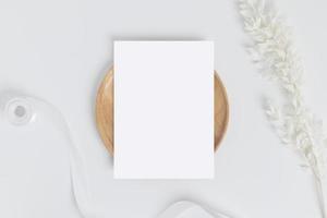 Greeting card or invitation card with white dry flower leaves on wood plate or tray in white background, top view photo