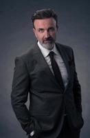 Portrait of a stylish elegant senior businessman with a beard and casual business clothes in photo studio isolated on dark background gesturing with hands