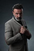 Portrait of a stylish elegant senior businessman with a beard and casual business clothes in photo studio isolated on dark background gesturing with hands