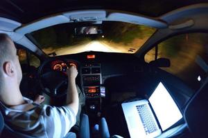 man working on laptop while drivig car on night photo