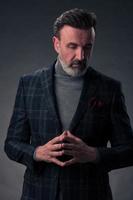 Portrait of a stylish elegant senior businessman with a beard and casual business clothes in photo studio isolated on dark background gesturing with hands