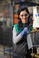 mujer trabajadora con gafas de seguridad controla la máquina de torno para perforar componentes. fábrica de fabricación industrial de torno de metal foto