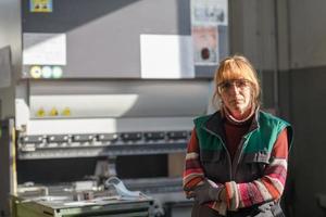 retrato de una mujer parada frente a una máquina cnc con gafas y trabajando en una moderna fábrica de producción y procesamiento de metales foto