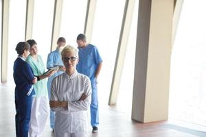 female doctor with glasses and blonde hairstyle standing in front of team photo