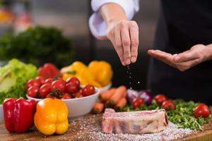 chef poniendo sal en una jugosa rebanada de bistec crudo foto