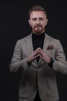 Portrait of a stylish elegant senior businessman with a beard and casual business clothes in photo studio isolated on dark background gesturing with hands