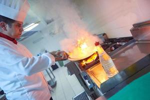 chef en la cocina del hotel prepara comida con fuego foto