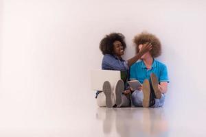 multiethnic couple sitting on the floor with a laptop and tablet photo