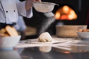 chef sprinkling flour over fresh pizza dough photo