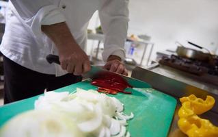 chef en la cocina del hotel cortar verduras con cuchillo foto