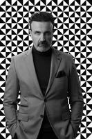 Black and white portrait of a stylish elegant senior businessman with a beard and casual business clothes against retro colorful pattern design background gesturing with hands photo