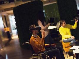 Disabled businessman in a wheelchair at work in modern open space coworking office with team using virtual reality googles drone assistance simulation photo