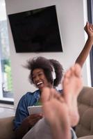 mujer afroamericana en casa en silla con tableta y auriculares foto