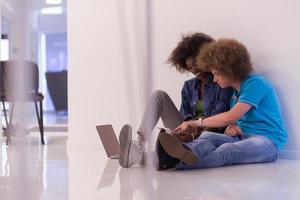 multiethnic couple sitting on the floor with a laptop and tablet photo