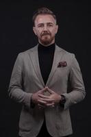 Portrait of a stylish elegant senior businessman with a beard and casual business clothes in photo studio isolated on dark background gesturing with hands